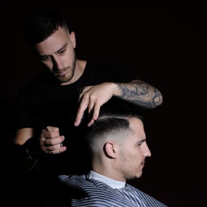 Foto con fondo negro del barbero cortando el pelo